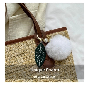 Detail of white faux fur pompom and green leaf charm with pearl on woven tote bag