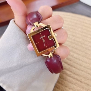 Close-up of the square golden watch case and deep red dial on a leather wristband