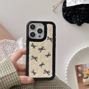 Detail of plush fleece iPhone case with black embroidered bow on cream fabric texture