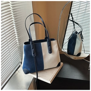 Detail of contrast color denim tote bag with leather straps on a natural light background