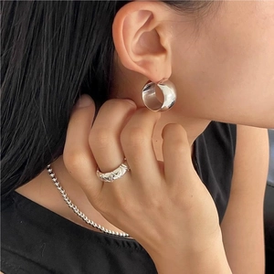 Detail of silver C-shape hoop earrings and textured ring set on female model