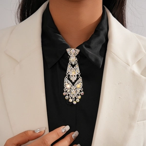 Detailed close-up of a silver tassel brooch with rhinestones worn on a white blazer suit