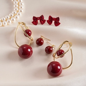 Detail of vintage burgundy bow and geometric pearl stud earrings on beige satin fabric