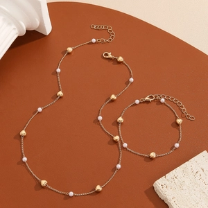 Fashionable gold heart necklace and bracelet set with white pearls on a textured background