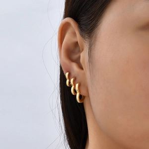 Close-up of three gold wave hoop earrings worn together for a modern layered ear look