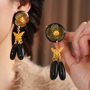 Close-up of vintage black agate and gold butterfly drop earrings worn by a model