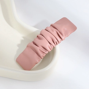 Detail of pink ruched PU leather hair clip on a minimalist white ceramic tray