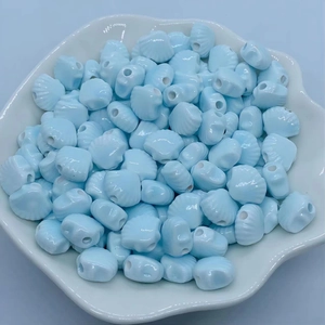 Macro shot of light blue shell-shaped ceramic beads in a white decorative tray