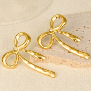 Detail of 18k gold butterfly bow dangle earrings on a textured stone pedestal
