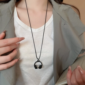 Close-up of a black headphone pendant necklace worn over a casual grey outfit