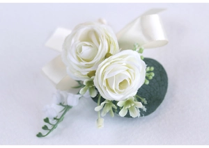 Close-up of cream white artificial rose boutonniere with beige satin bow and green leaves
