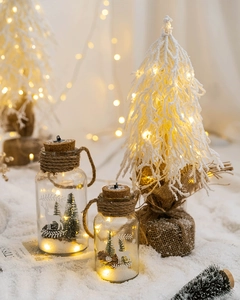 Close-up of a warm LED glass bottle night light with a miniature reindeer and snowy tree