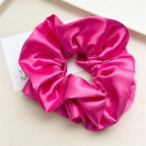 Close-up of vibrant rose red satin scrunchie with soft pleated texture and silk sheen