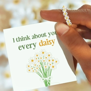 Close-up of daisy chain ring held with a romantic greeting card in a floral setting