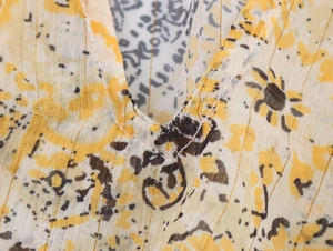 Macro detail of V-neckline on yellow floral chiffon fabric with woven metallic threads