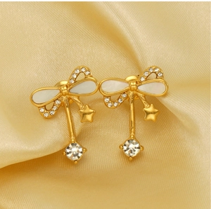 Detail of gold bow earrings with white shell inlay, star charms and crystal tassels