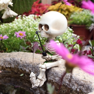 Close-up of resin skeleton figurine fishing on a rock with garden floral background