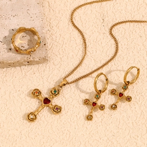 Golden cross jewelry set with red heart crystals on minimalist stone background