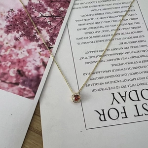 Detail of a gold necklace with a red zircon pendant on a decorative card background