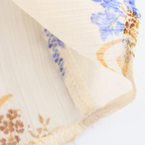 Dettaglio del tessuto in chiffon beige con fiori blu e cuciture dell'orlo rifinite