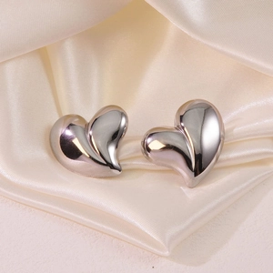 Minimalist silver heart stud earrings with glossy finish on cream silk fabric