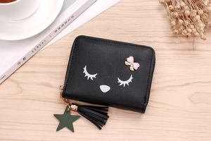 Detail of cute black cartoon wallet with tassel and bow on light wood surface