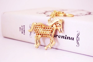 Detail of a golden alloy running horse keychain resting on a white book surface