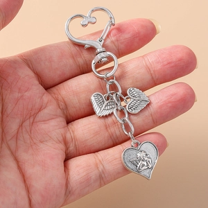 Silver angel wings and heart rhinestone keychain held by hand on a beige background