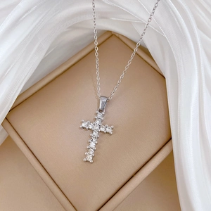 Macro detail of a silver zircon cross pendant necklace on elegant white silk background