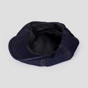 Gros plan sur casquette gavroche en denim bleu avec surpiqûres orange et doublure noire
