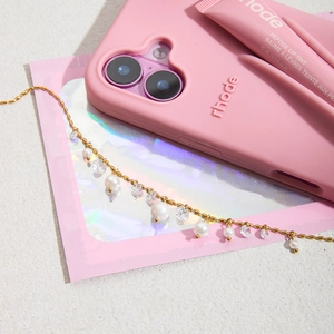 Detail of a gold chain bracelet with pearls and crystals on pink aesthetic packaging