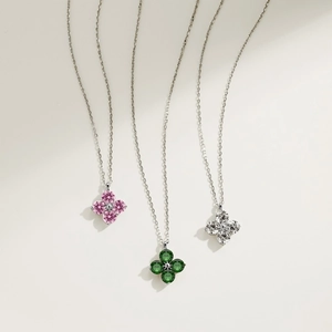 Detail view of silver necklaces with pink, green, and white চার-leaf clover stone pendants