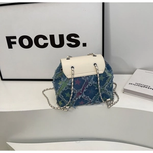 Detail of denim backpack with star embroidery and metallic chain strap on a white stand