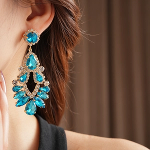 Close-up of elegant gold tassel earrings with blue rhinestones worn by a model