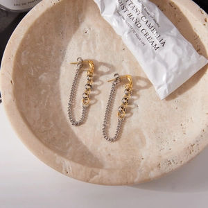 Détail de boucles d'oreilles pampilles bicolores or et argent sur plateau en pierre