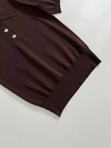 Detail of the golden flower-shaped button with pearl on a dark brown knit polo shirt