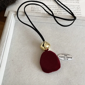Detail of dark red flocked resin pendant with gold geometric link on a black cord