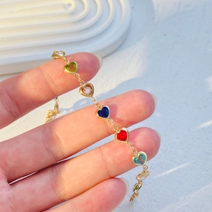 Macro detail of heart-shaped multi-color gemstone gold chain bracelet worn on hand