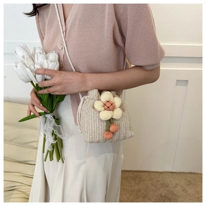 Dettaglio di una mini borsa a secchiello in paglia con fiori e pompon rosa