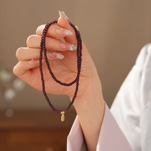 Elegant multi-strand dark red garnet beaded bracelet with a gold Fu pendant on model hand