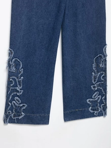 Détail de la broderie florale effilochée sur le bas d'un jean bleu marine à coupe large