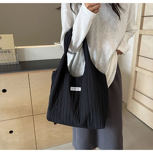 Details einer schwarzen Nylon-Schultertasche mit KISS YOURSELF Label und Faltenstruktur