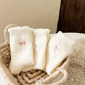 White plush socks with pink bow embroidery in a woven basket for home winter warmth