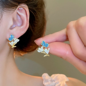 Close-up of blue butterfly and white flower stud earrings with elegant gold leaf details