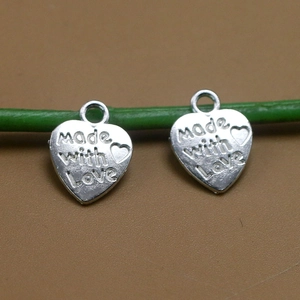 Vista macro de colgantes de corazón plateados grabados con Made with Love para joyas DIY
