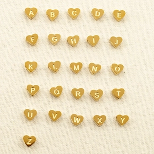 Golden heart-shaped titanium steel alphabet charms with A-Z engravings on beige fabric