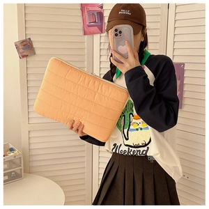 Lifestyle shot of an orange quilted laptop sleeve with stylish horizontal stitching