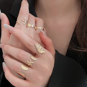 Macro shot of gold starfish and shell rings set on a model's hand with black suit