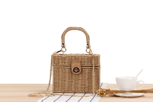 Close-up of woven straw box bag with brown leather strap and gold metal lock detail
