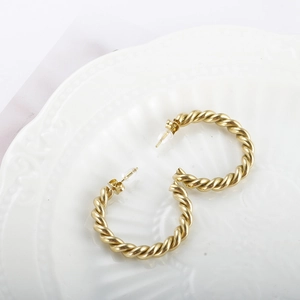 Détail de boucles d'oreilles créoles torsadées dorées avec une finition mate